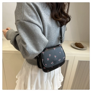 Detail view of small black PU leather shoulder bag with vibrant red cherry print accents