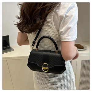 Detail of black box bag showing textured woven flap and golden circular twist lock buckle