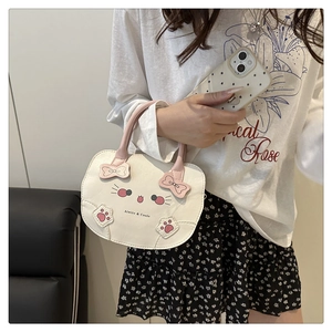 Detalle de un bolso blanco con forma de gato, asa rosa y decoración de lazo