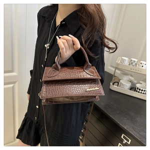 Detail of dark brown crocodile texture crossbody bag with gold metal logo and handle