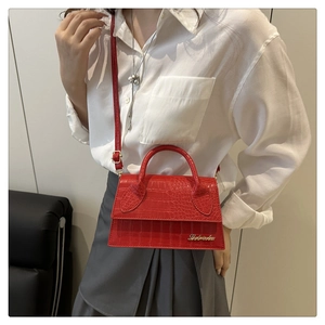 Detail of red crocodile textured leather bag with gold logo and elegant shoulder strap