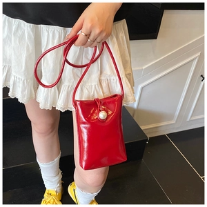 Detail of red patent leather bucket bag with a prominent white pearl clasp closure