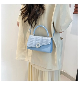 Detail of light blue crossbody bag with heart buckle and woven textured flap