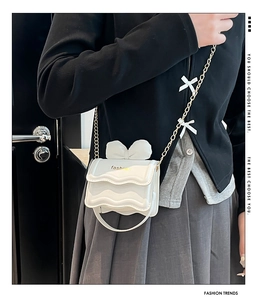 Détail du mini sac blanc avec nœud, bords festonnés et bandoulière chaîne dorée