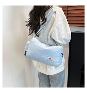 Detail view of a light blue canvas barrel bag worn by a model in a minimalist room