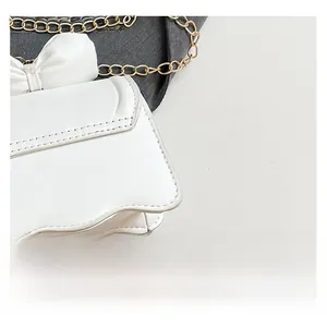 Détail d'un sac porté épaule en cuir blanc avec nœud décoratif et chaîne dorée