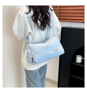 Detail showing back view of light blue canvas cylinder crossbody bag worn by a model