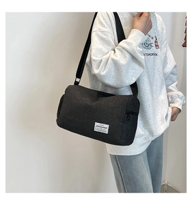 Detail of minimalist black canvas crossbody bag with white woven label on the front corner