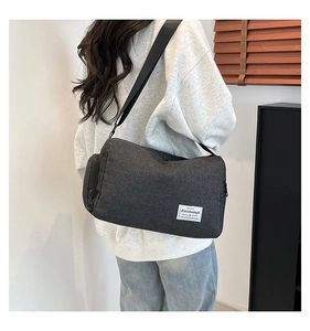 Detail view of large dark grey canvas crossbody bag worn by model in a minimalist setting