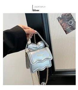 Gros plan d'un mini sac argenté avec nœud papillon, rabat ondulé et chaîne dorée