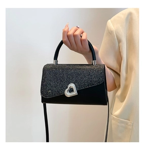 Detail of black glitter crossbody bag with large silver heart-shaped metal buckle closure