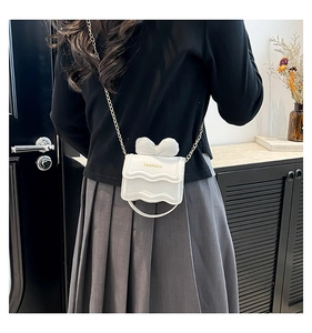 Détail du mini sac blanc à chaîne avec nœud décoratif et bandoulière dorée sur modèle