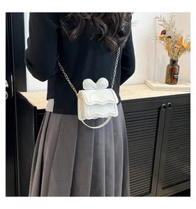 Vue détaillée du mini sac blanc à nœud avec bandoulière dorée porté par un mannequin