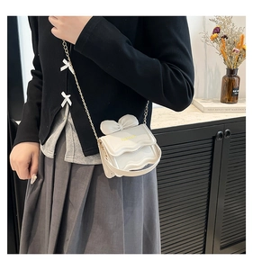 Détail du mini sac crème avec nœud décoratif, bord ondulé et chaîne dorée chic