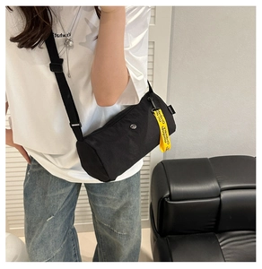 Détail du sac bandoulière cylindrique noir avec une sangle jaune lettrée contrastée