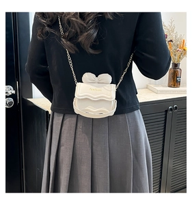 Détail d'un mini sac crème avec nœud 3D et chaîne dorée porté par un mannequin