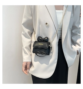 Détail du sac en cuir PU noir avec nœud et chaîne dorée sur un blazer blanc
