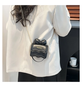 Détail d'un mini sac à bandoulière noir avec chaîne dorée et décoration nœud élégant