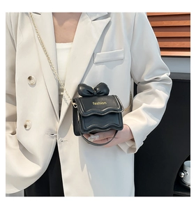 Mini sac bandoulière noir avec nœud et chaîne dorée porté sur un blazer blanc chic