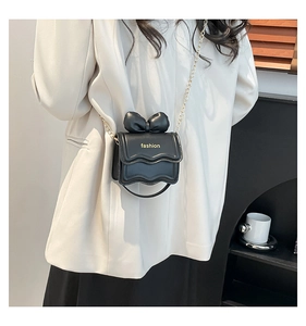 Mini sac noir à rabat ondulé et nœud doré porté sur une veste de costume blanche