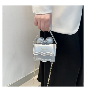 Mini sac à main argenté métallisé avec nœud et chaîne dorée tenu par un mannequin