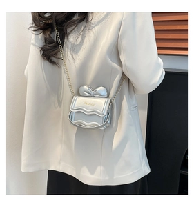 Détail d'un mini sac argenté avec décoration de nœud et bandoulière chaîne dorée