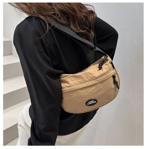 Detail view of beige nylon crescent bag with Lucky Fashion patch on a model's back