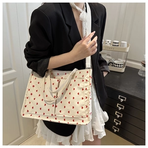 Detail of cream corduroy tote bag with red heart prints and wide woven strap on model