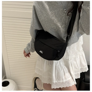 Detail showing the adjustable wide strap and round logo on black crescent crossbody bag