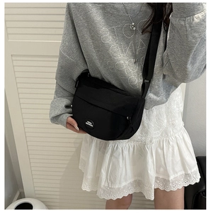 Detail of black crescent crossbody bag showing the round logo and adjustable strap texture