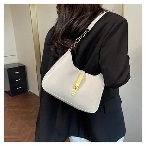 Detail of minimalist cream square shoulder bag with gold hardware and chain strap on a black blazer
