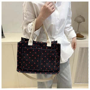 Detail of navy corduroy tote bag with red heart patterns and canvas straps on shoulder