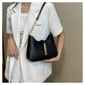 Detail of minimalist black leather shoulder bag with golden metallic bar and chain strap