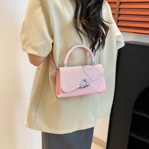 Pink sequin crossbody bag with heart buckle shown on model in a home setting