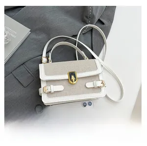 Detail of a two-tone crossbody bag with gold buckle on a blazer next to a smartphone