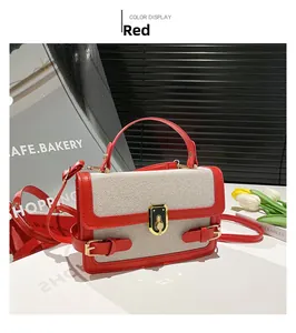 Detail of a color-block handbag featuring red leather trim and a gold metal twist lock closure
