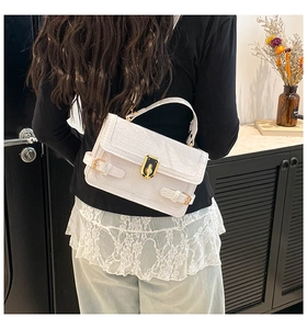 Detail of white crocodile pattern shoulder bag featuring golden turn-lock clasp and strap