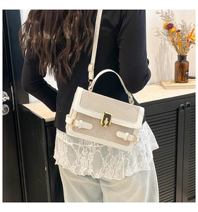 Detail view of stylish cream-colored leather and canvas handbag with gold twist lock