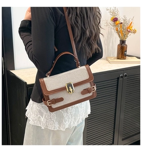 Detail of canvas handbag with brown leather trim and vintage gold lock on a marble table
