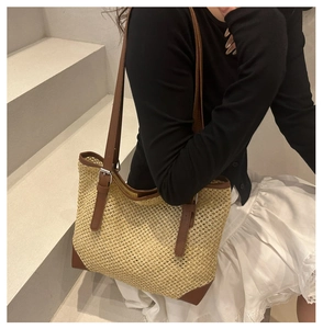 Detail of woven straw tote bag featuring brown leather trim and metal buckle on strap