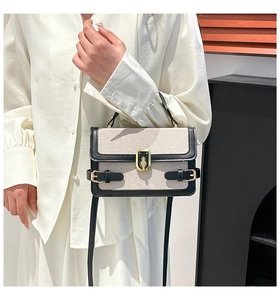 Close-up of a cream canvas handbag with black leather trim and a gold twist lock clasp