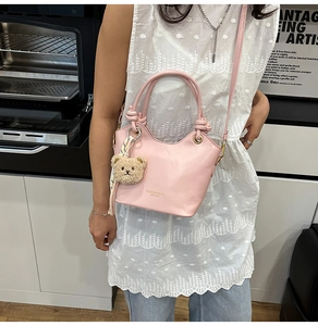 Pink leather bucket bag detail with golden text and cute teddy bear charm accessory