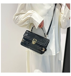 Detail of black crocodile texture handbag with glossy finish and gold metal hardware