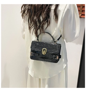 Detail of a black faux crocodile leather crossbody bag with a gold metal twist lock buckle