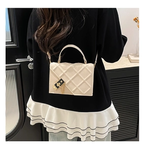 Detail of cream quilted crossbody bag with gold chain strap and black square buckle closure