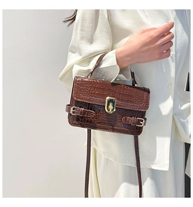 Detail of dark brown crocodile pattern handbag featuring a gold buckle and textured finish