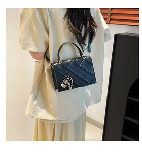 Detail of a black quilted crossbody bag featuring metal hardware and chain on model