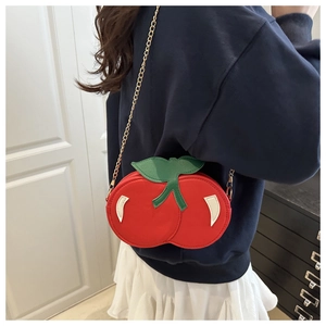 Detail of red cherry crossbody bag with green leaf accents and gold chain strap
