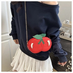 Detail of red cherry crossbody bag with leaf accent and gold chain strap on a model
