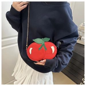 Close-up of a stylish red cherry shaped crossbody bag with gold chain strap on a model